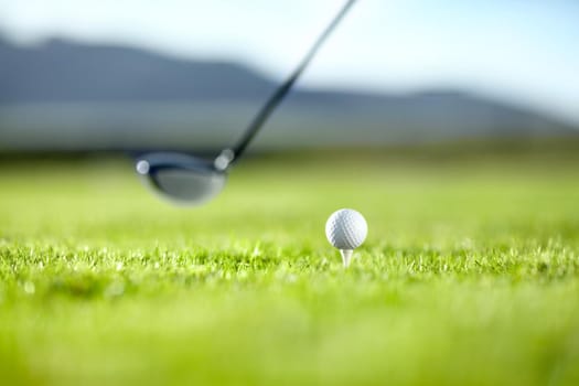 A golf club ready to tee-off with a white ball on a golf course.