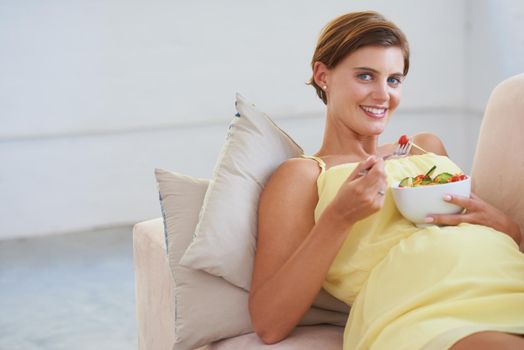 Taking her babys health into concern - Diet. Portrait of a young pregnant woman enjoying a healthy salad while relaxing on the couch.