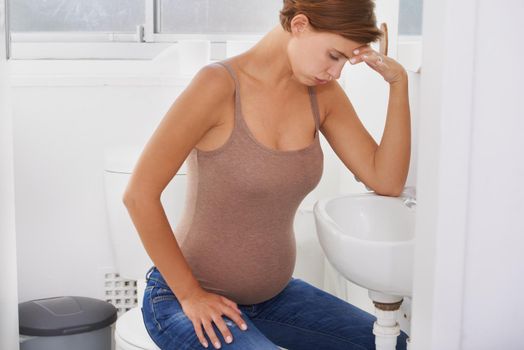 Riding waves of nausea. A pregnant woman struggling with morning sickness in the bathroom.