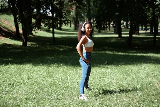 young woman with headphones does gymnastics in the park.