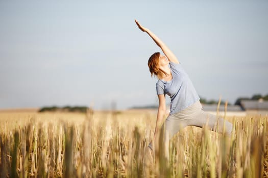 Shot of an attractive woman doing yoga in a crop field.