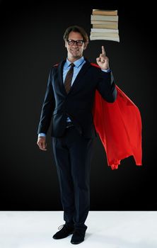 Balancing the books like a hero. Shot of a businessman wearing a red cape hovering books over his finger.