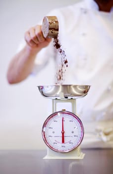 Precision makes perfection. Shot of a baker weighing a cup of cocoa powder on a scale.