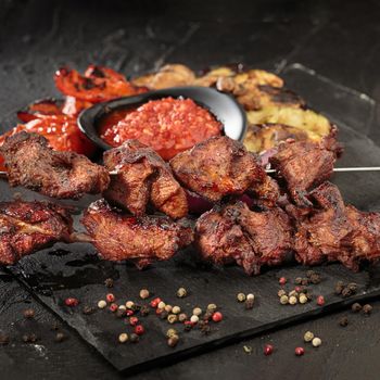 Shashlik or shish kebab preparing on barbecue grill over hot charcoal. Grilled pieces of pork meat on metal skewers. Square image