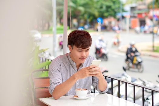 Young smiling man looking on the phone or reading message in cafe outdoor