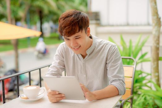 Front view portrait of a happy man holding tablet sitting in a coffee shop