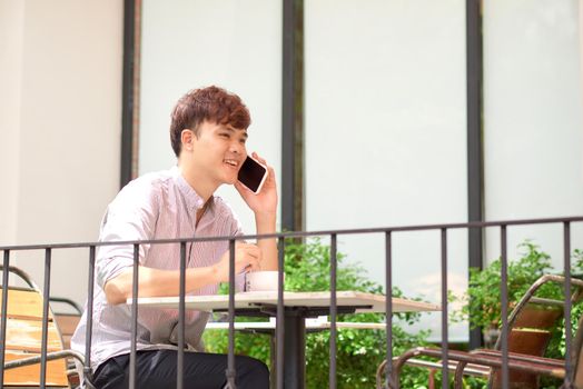 Young man in coffee shop talking on the phone. Outdoors
