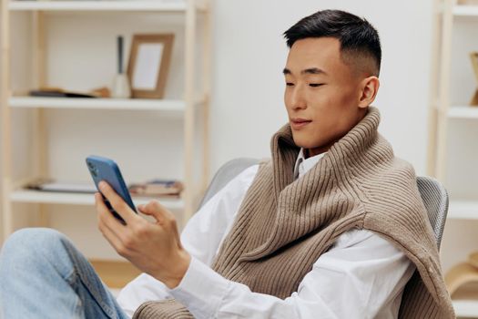 Asian man sitting in a chair in a room with phone on his lap