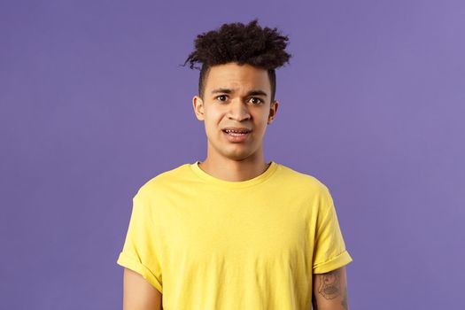 Waist-up portrait of young concerned hispanic man with worried gaze looking at camera, frowning being scared for friend stuck in troublesome situation, want help, stand purple background