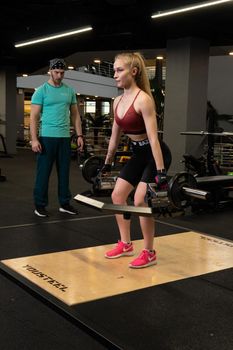 RUSSIA, MOSCOW - FEB 11, 2022: Instructor and client girl deadlift blonde trap bar personal exercise, for lifestyle lifting for person and sport strength, concept couple. Working female bodybuilding, training