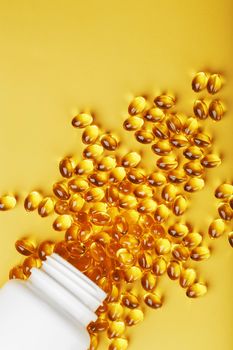 Golden Omega-3 fish oil capsules poured out of a jar on a yellow background