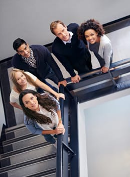 Looking down upon the dream team. Portrait of a group of office coworkers standing in a stairwell.