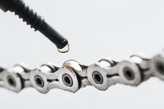 Greasing a bicycle chain with a drop of golden oil close-up on a gray background
