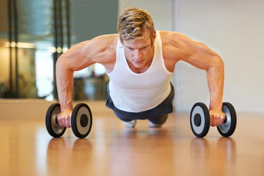 Working his arms and back. Fit young man doing push ups in a health club using dumbbells.