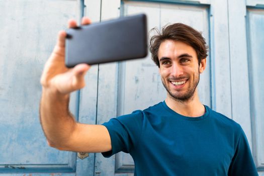 Young caucasian man taking a selfie with smartphone outdoors. Selective focus on face.