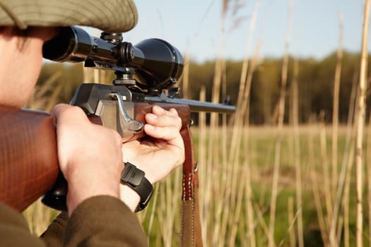 Patience is the secret to a perfect shot. A game hunter looking through the reeds with his sniper rifle.