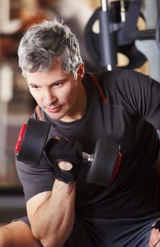 Defining his biceps. A mature man doing bicep curls with a dumbbell at the gym.