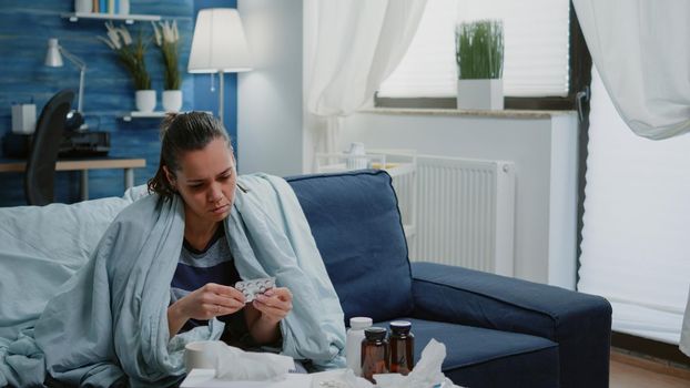 Sick woman looking at bottle of pills and tablets with capsules