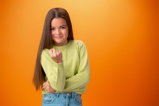 Teen girl showing off muscles biceps against orange background
