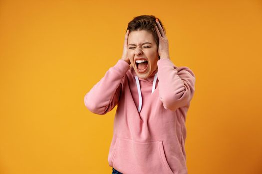 Portrait of very frustrated and angry screaming woman against yellow background