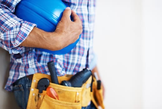 Construction worker holding protective helmet. Mid section of construction worker with tool belt holding blue protective helmet.