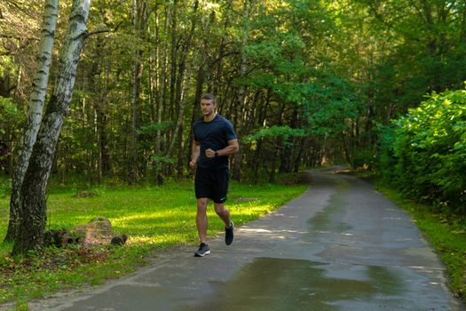 A man athlete runs in the park outdoors, around the forest, oak trees green grass young enduring athletic athlete run sport nature, lifestyle jogger endurance person man. Adult energy feet stretches