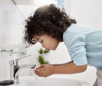 Staying clean and fresh. Shot of an adorable little boy washing his hands and mouth at a tap in a bathroom at home.