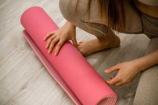 Yoga at home woman rolls pink exercise mat in living room starting to warm up meditation zen well being lifestyle living room apartment.