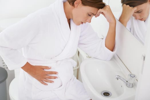 Struggling with morning sickness. A pregnant woman struggling with morning sickness in the bathroom.
