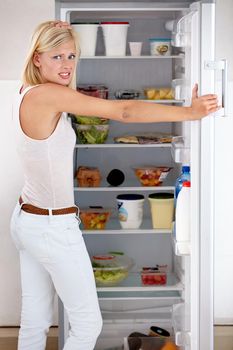 Tempted to cheat on her diet. Portrait of a worried young woman looking in her fridge.