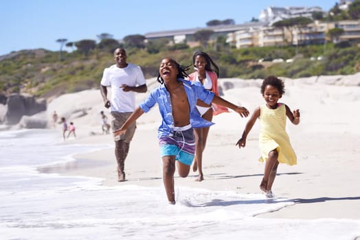Nothing beats a family vacation. A happy young african family running energetically along the beach.