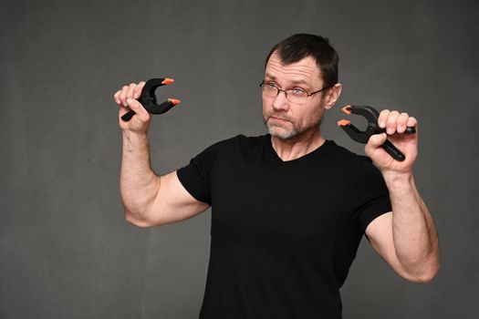 An adult man in glasses and a black t-shirt shows wire cutters on a gray background.