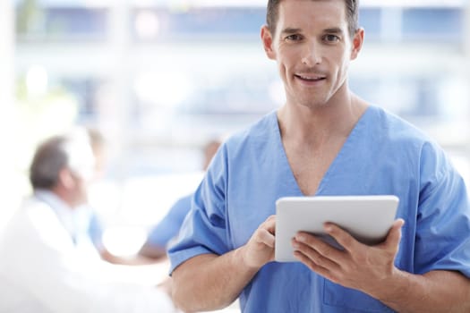 Digital doctor. A medical professional working on a touchpad with colleagues sitting in the background.