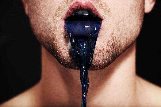 The colour of lies. Closeup of a young mans mouth spitting out purple liquid.