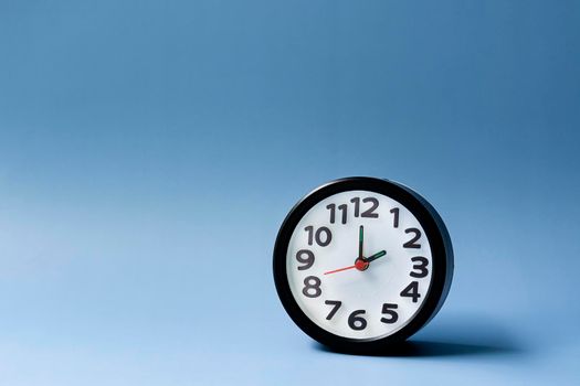 Black alarm clock isolated on blue background. The clock set at 2 o'clock.
