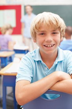 He loves class. Portrait of a cute blonde schoolboy in sitting at a desk in class.