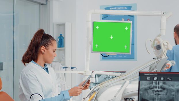 Dentist analyzing horizontal green screen on monitor and radiography of teeth for dental care. Woman using chroma key and mockup template for oral examination and teethcare in cabinet.