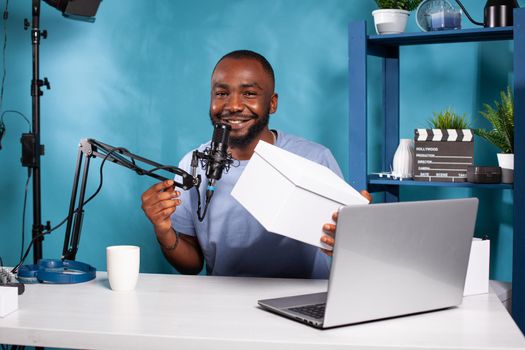 Smiling vlogger holding white box in vlogging studio with professional live setup