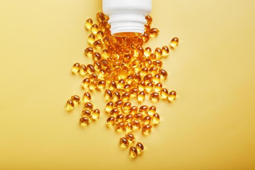 Gold Vitamin D3 capsules poured out of a jar on a yellow background with free space