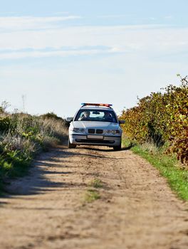 Police patrol. Shot of a police car driving down a dirt road.