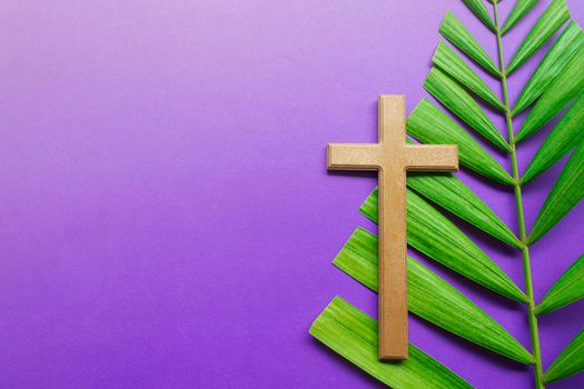 Cross and palm leaves on purple background. Lent season concept.