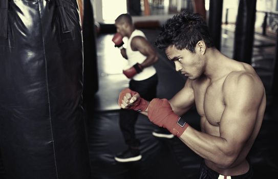Hes dedicated to the sport of boxing. Shot of a young male boxers training on heavy bags.