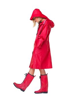 Why does it always rain on me. Woman wearing a red raincoat, hat and boots with her head looking down and hands in her pockets- full length.