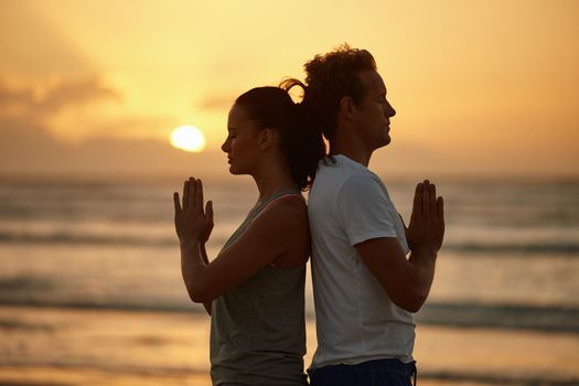 Soul experience at sunset. Shot of a couple doing yoga on the beach at sunset.