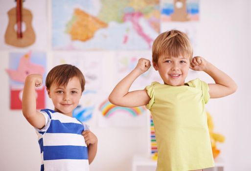 He wants to be just like his big bro. Two young boys flexing their muscles while standing in their bedroom.