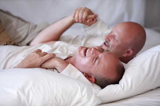 All you need is love. Playful homosexual couple frolicking on their bed of white linen.