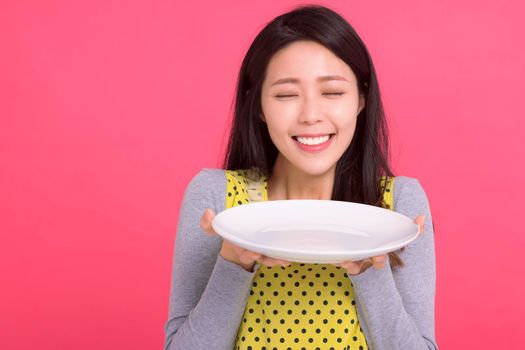 Happy young woman holding empty white plate and smelling