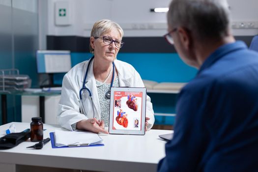 Physician explaining cardiology diagnosis with image of heart organ on tablet to patient