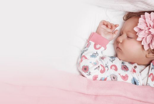 Portrait of an Adorable Baby Girl With Cute Pink Flower Hairpin Peacefully Sleeping in the Crib at Home. Photo with Copy Space. Healthy Babies Life Concept.
