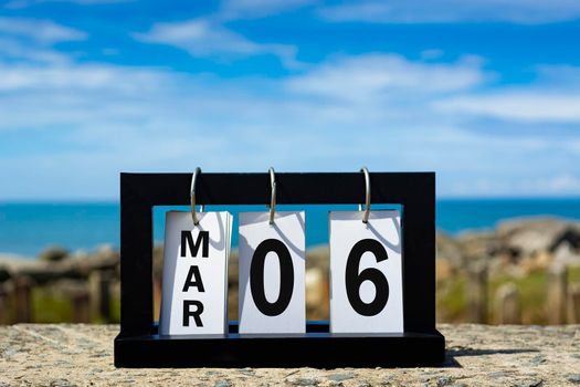 Mar 06 calendar date text on wooden frame with blurred background of ocean